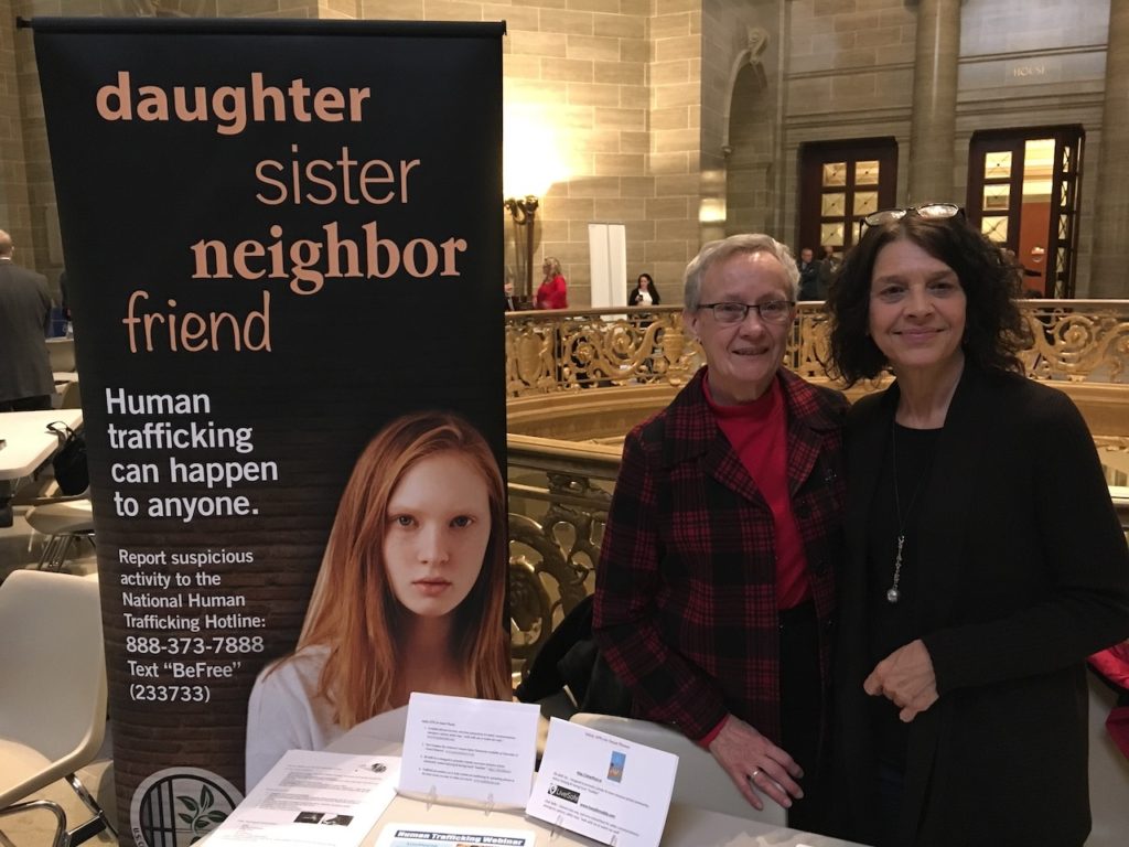 Two women stand next to a human trafficking sign in a government building